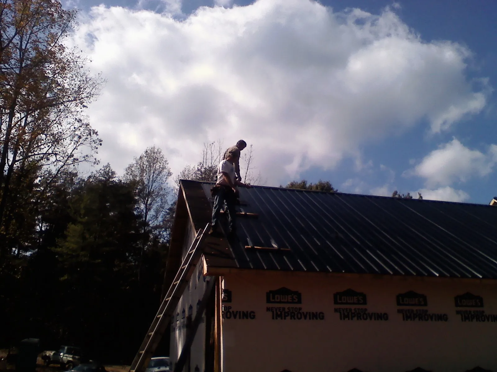 Roofer fastening dark metal panels high against a cloudy sky, from a Roof Inspection job in Bennett