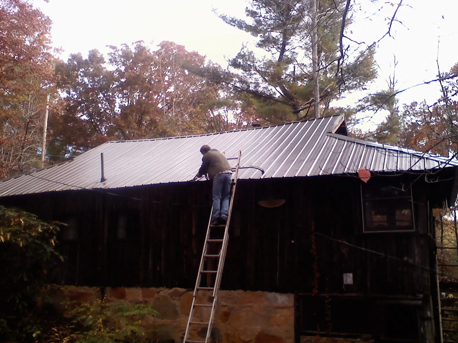 Roofer on a ladder working along the edge of a cabin metal roof in Bennett