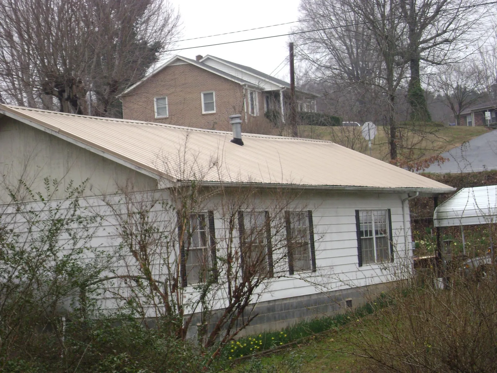 Tan metal roof on a white sided house set into a hillside — Commercial Roofing by Roofing Brothers in Bennett