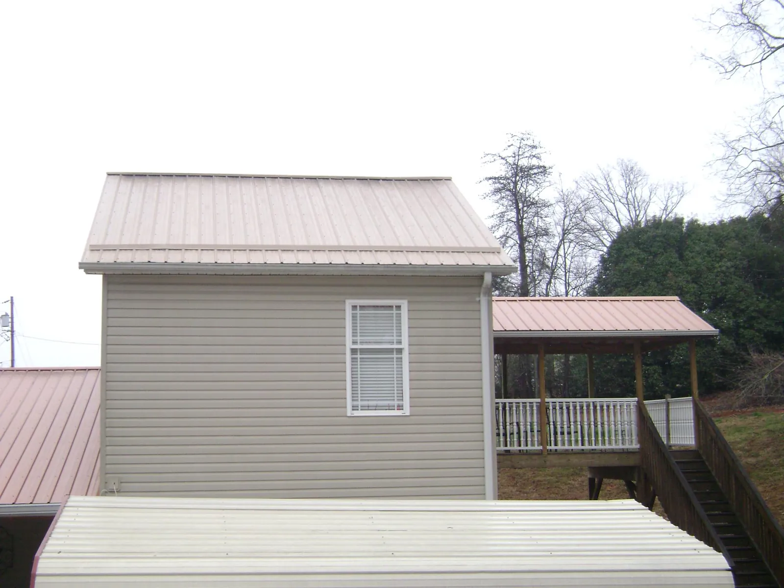Tan metal roofs on a two story addition and attached porch, from a Roof Replacement job in Bennett